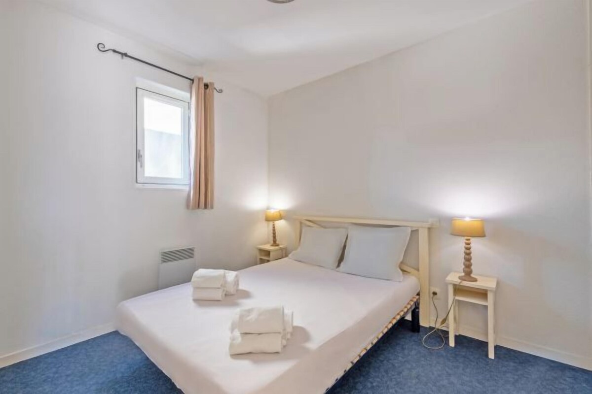 A hotel room with a single bed, two bedside lamps, a window with curtains, and a small bedside table.