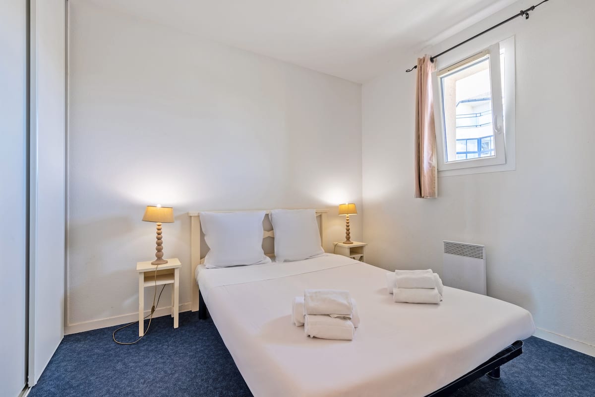 A hotel room with a single bed, two bedside tables with lamps, a window with curtains, and a radiator.