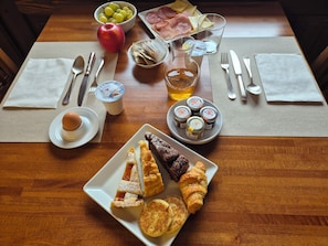 A breakfast table with a plate of pastries, a bowl of fruit, a glass of juice, and condiments.