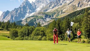 Een golfbaan met een bergachtige achtergrond, een vlaggenstok en spelers.