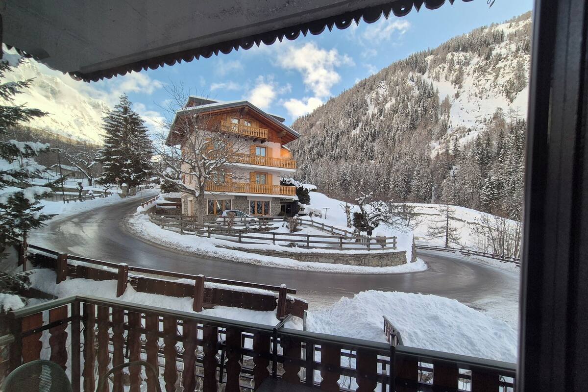 Un chalet de montagne avec une façade en bois, un balcon doté d’une balustrade et un paysage enneigé.