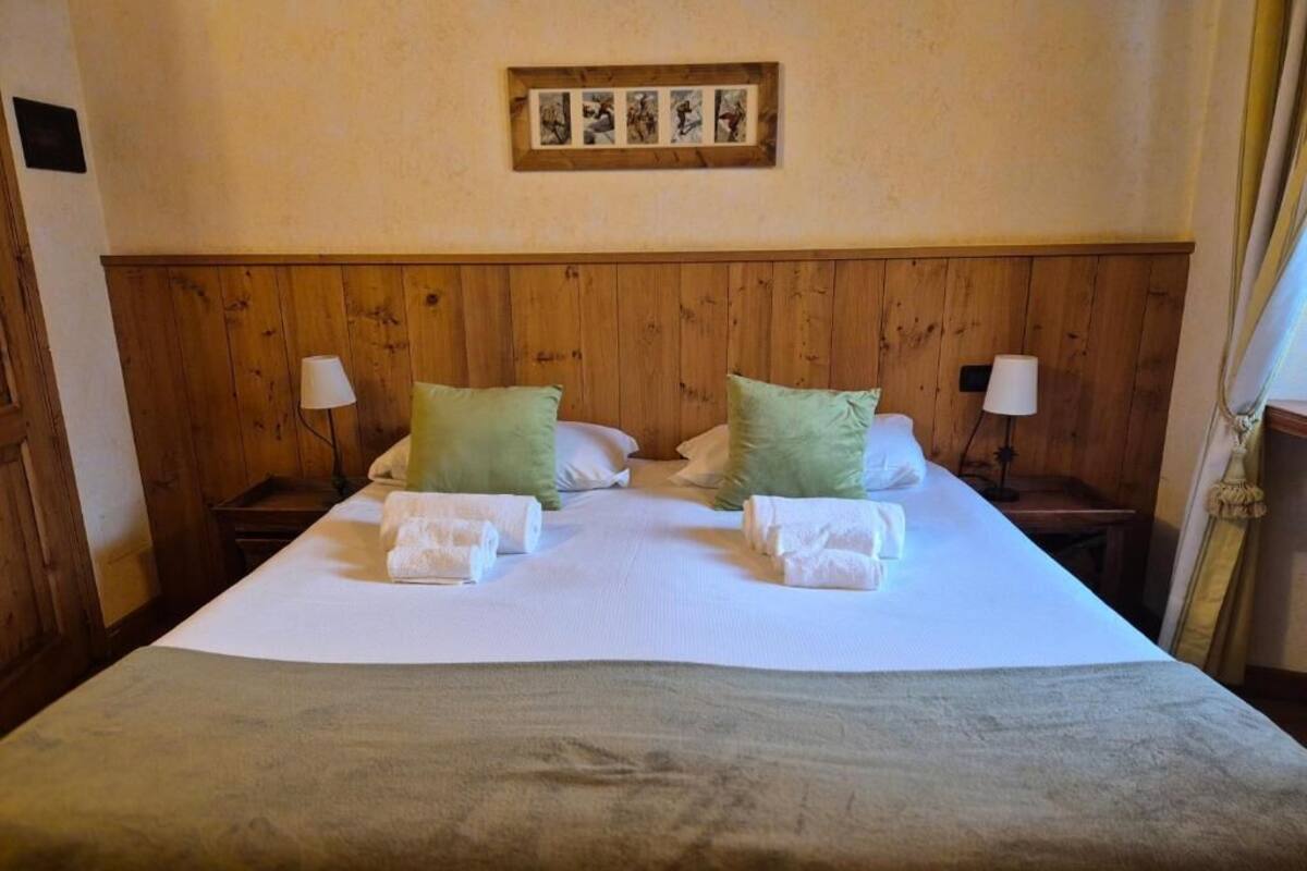 Un lit bien fait, avec des oreillers, une couverture et des serviettes, une tête de lit en bois, des tables de chevet avec des lampes et un tableau encadré au mur.