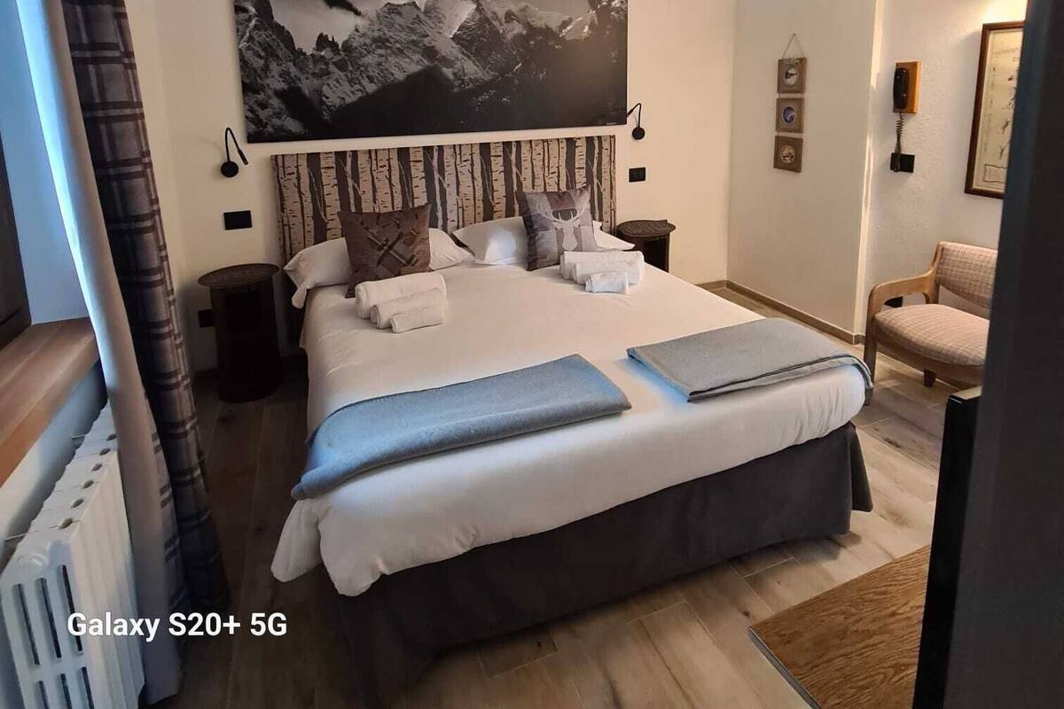 Une chambre spacieuse, décorée avec un Galaxy S20+ 5G, comprenant un grand lit, un tableau représentant un paysage de montagne et un fauteuil.