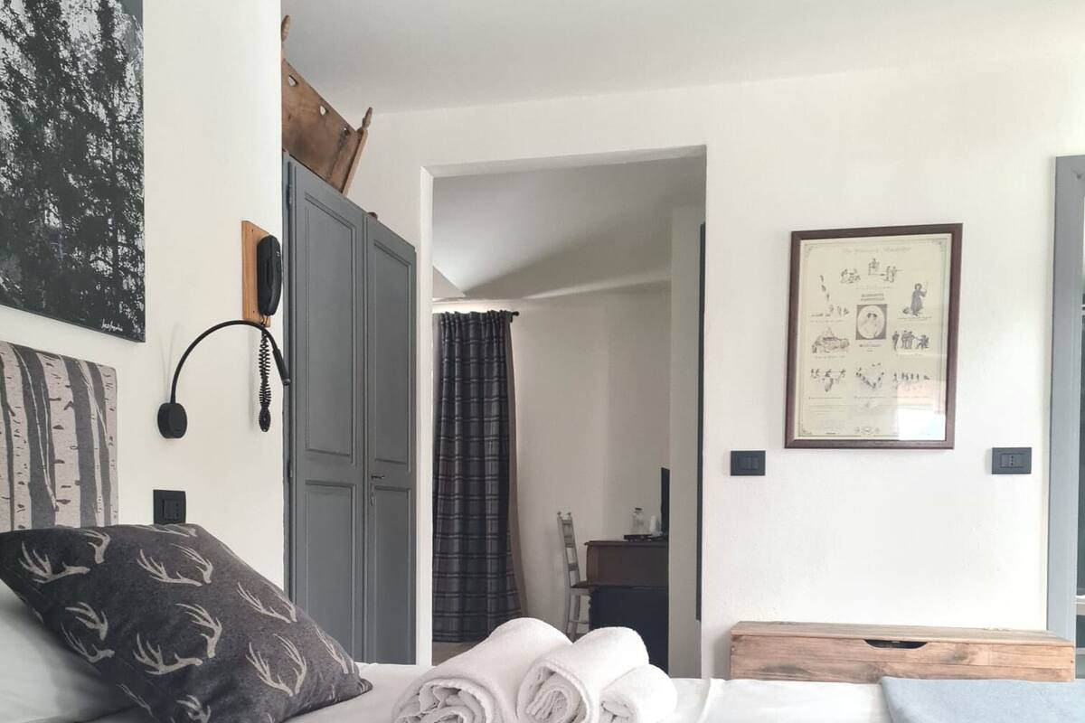 Un lit bien fait, avec des serviettes pliées, une armoire grise, un tableau encadré au mur et un téléphone sur la table de chevet.