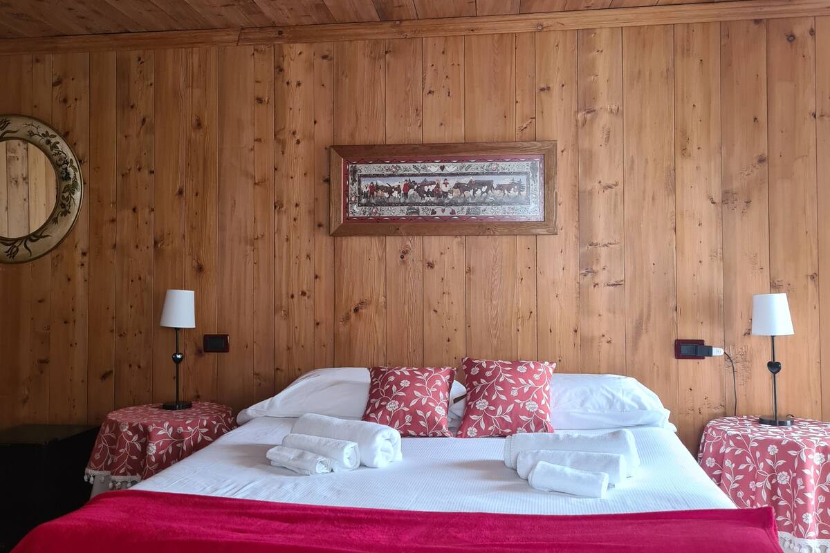 Une pièce aux murs lambrés, comprenant un lit, deux tables de chevet, deux lampes et un tableau encadré accroché au mur.