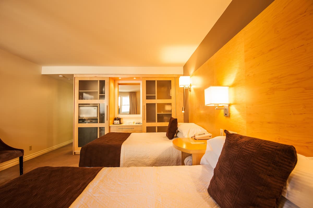 Ein Hotelzimmer mit zwei Betten, einem Schreibtisch, einem Spiegel und einem Kleiderschrank.