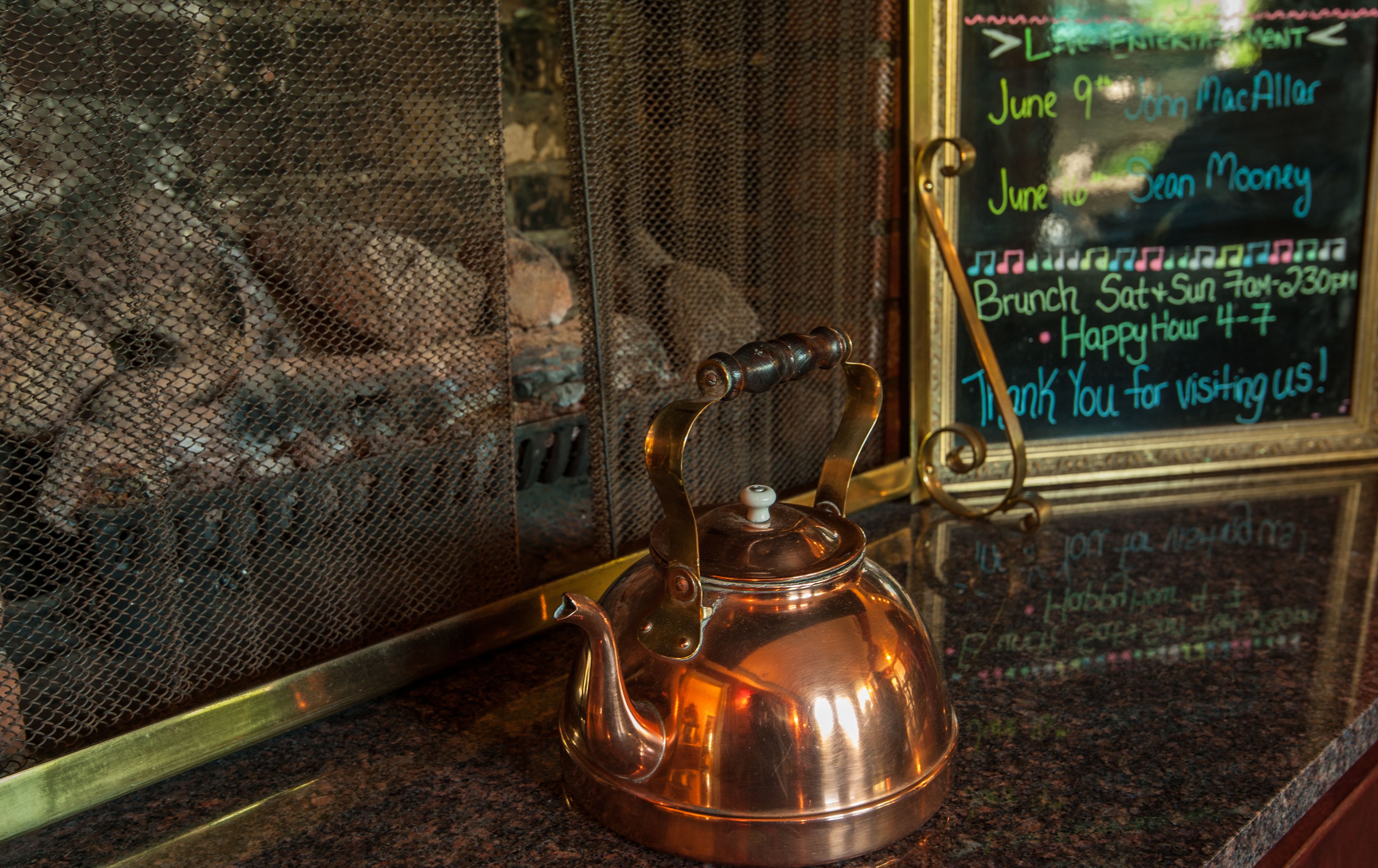 A copper teapot on a granite countertop with a metal mesh screen in the background.