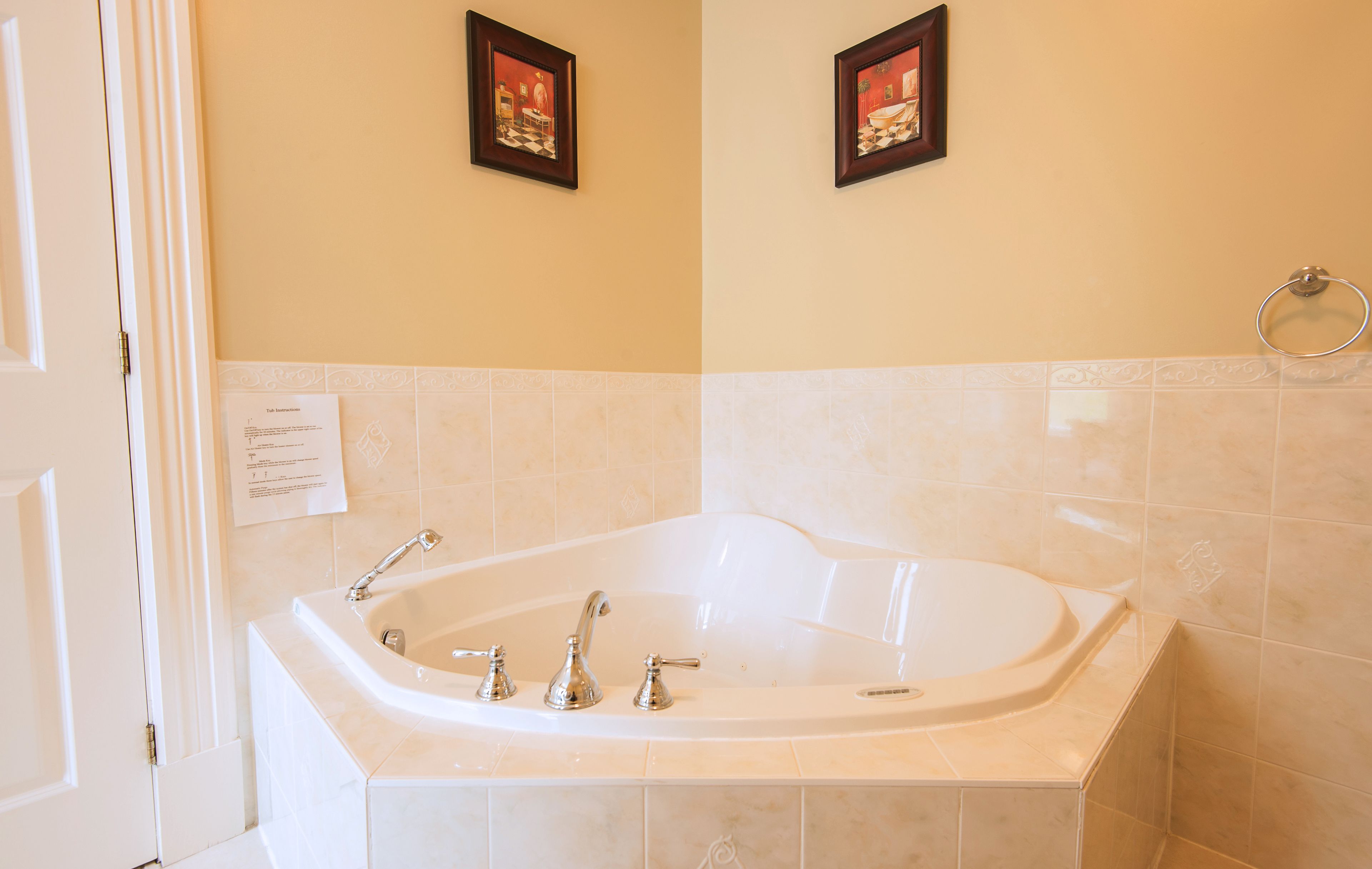 A bathroom with a large bathtub, two framed pictures on the wall, and a towel ring.