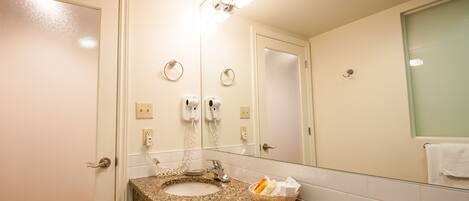 A bathroom with a granite countertop sink, a mirror, a towel rack, and a basket of toiletries.