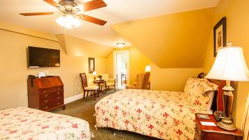 Une chambre d’hôtel avec deux lits, un ventilateur de plafond, une télévision, un bureau avec une lampe et une chaise.
