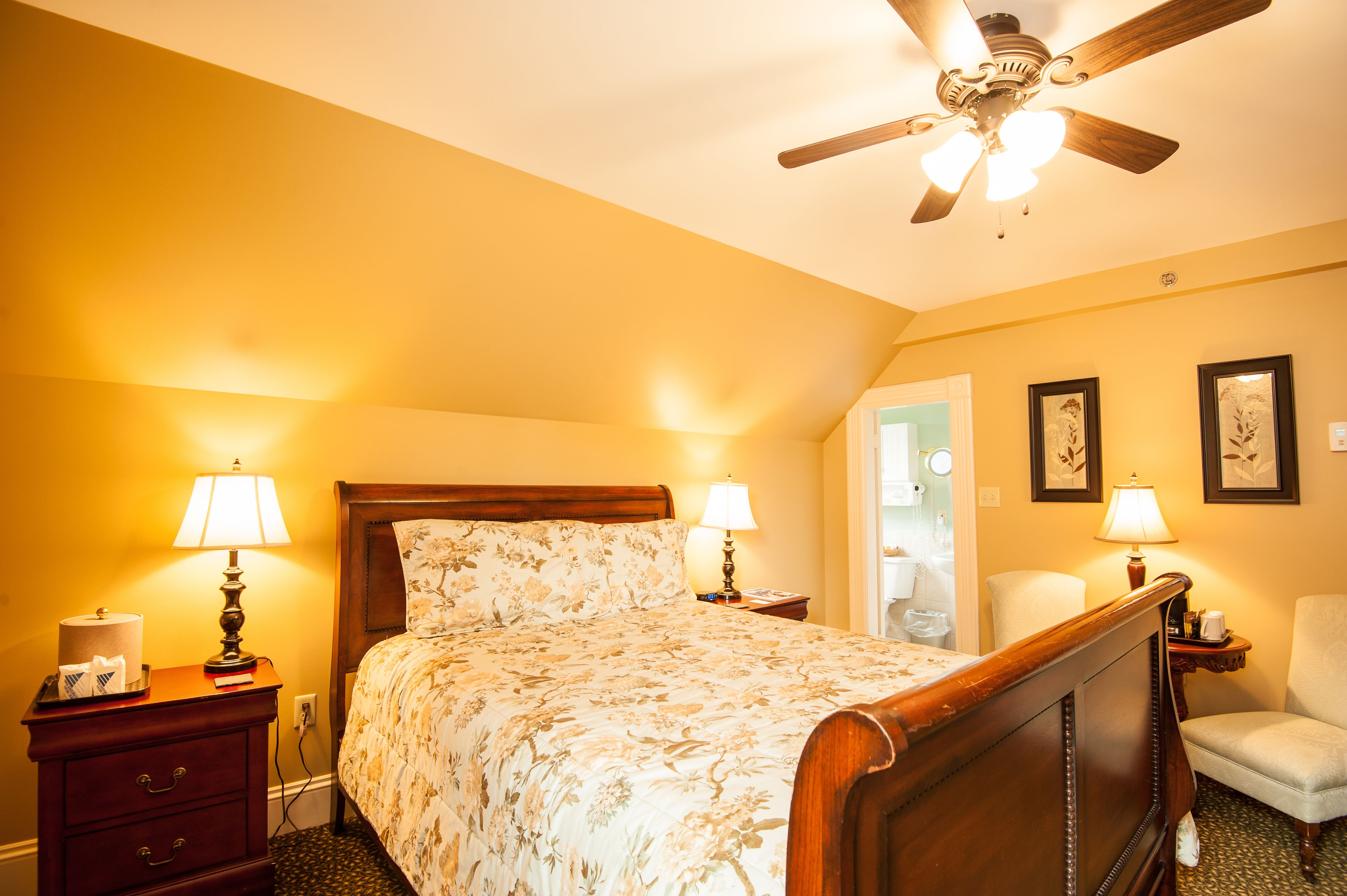 A hotel room with a wooden bed, two bedside lamps, a ceiling fan, and a chair.