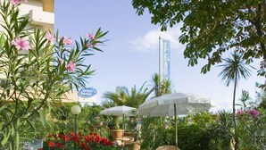 A hotel garden with red flowers, white umbrellas, and a sign for 'Hotel Bahia'. - Hotel San Giorgio Savoia (Bellaria-Igea Marina)