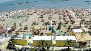 A beach with numerous umbrellas and sun loungers, a playground, and a building with outdoor seating. - Hotel San Giorgio Savoia (Bellaria-Igea Marina)