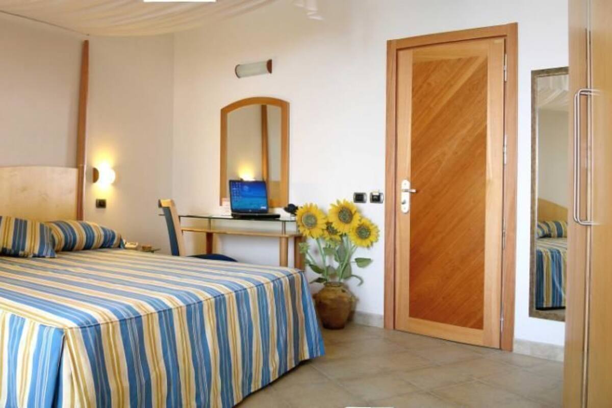 Une chambre à coucher avec un lit, un bureau avec un ordinateur portable, un miroir et une porte.
