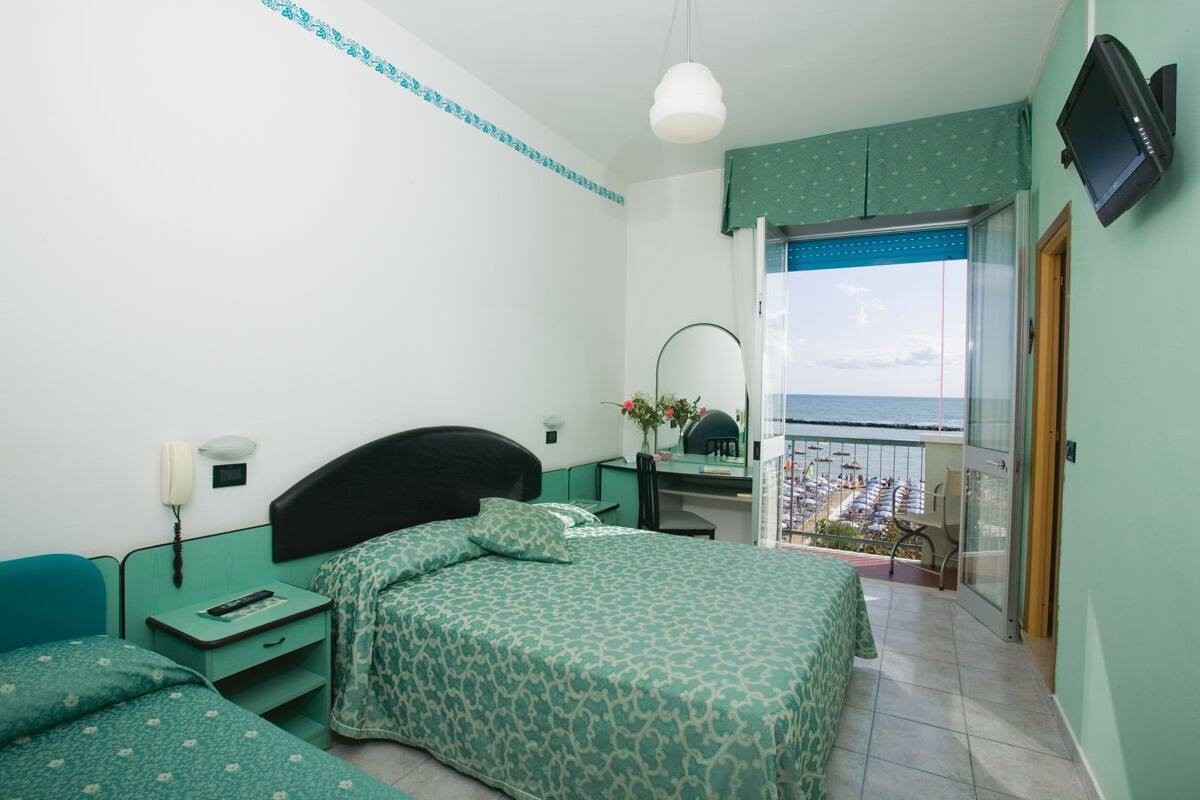 Une chambre à coucher avec un lit, une table de chevet et une vue sur un balcon équipé de chaises de plage.