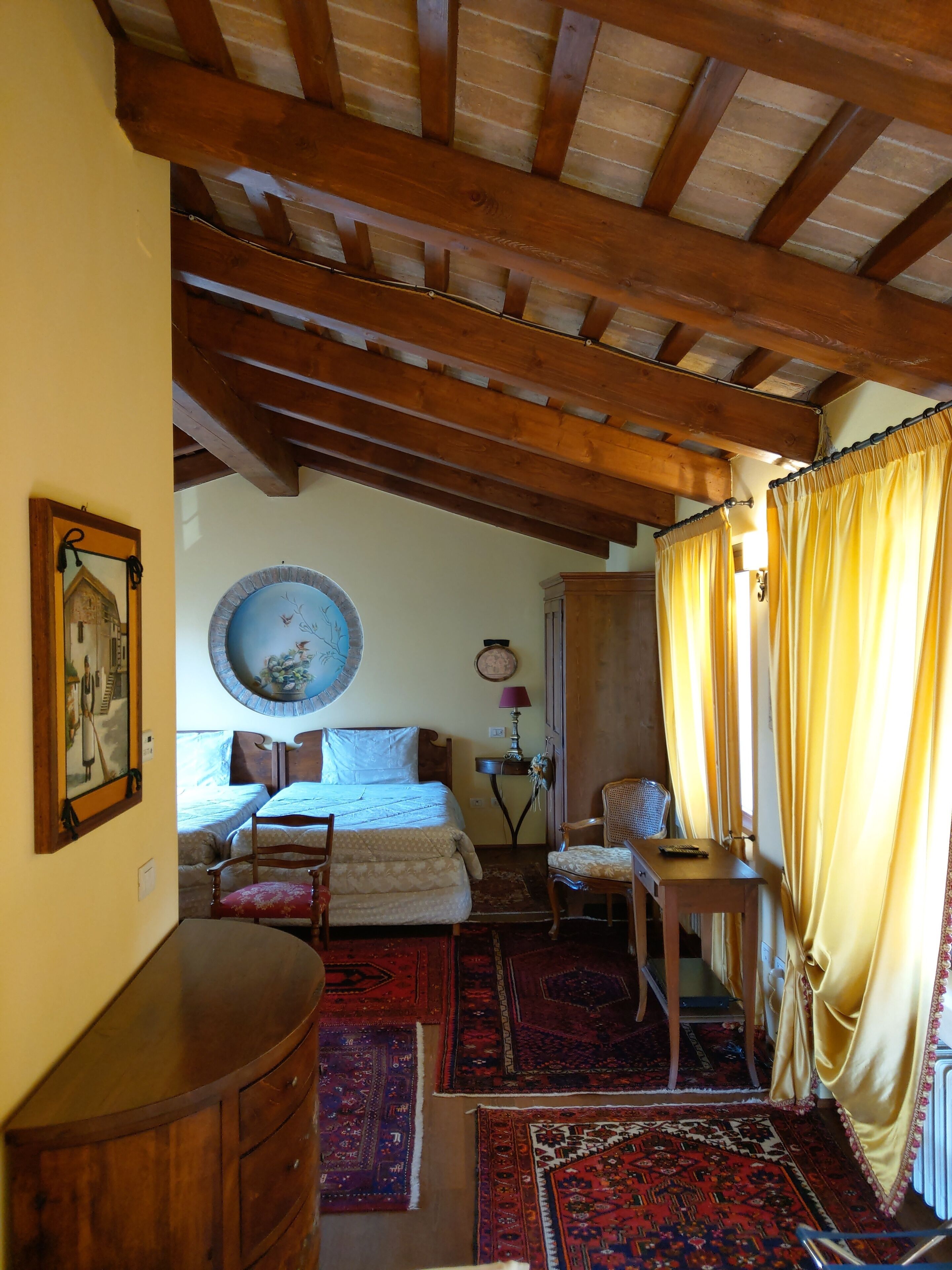 A room with a bed, two chairs, a table, a mirror, and a wall-mounted clock.