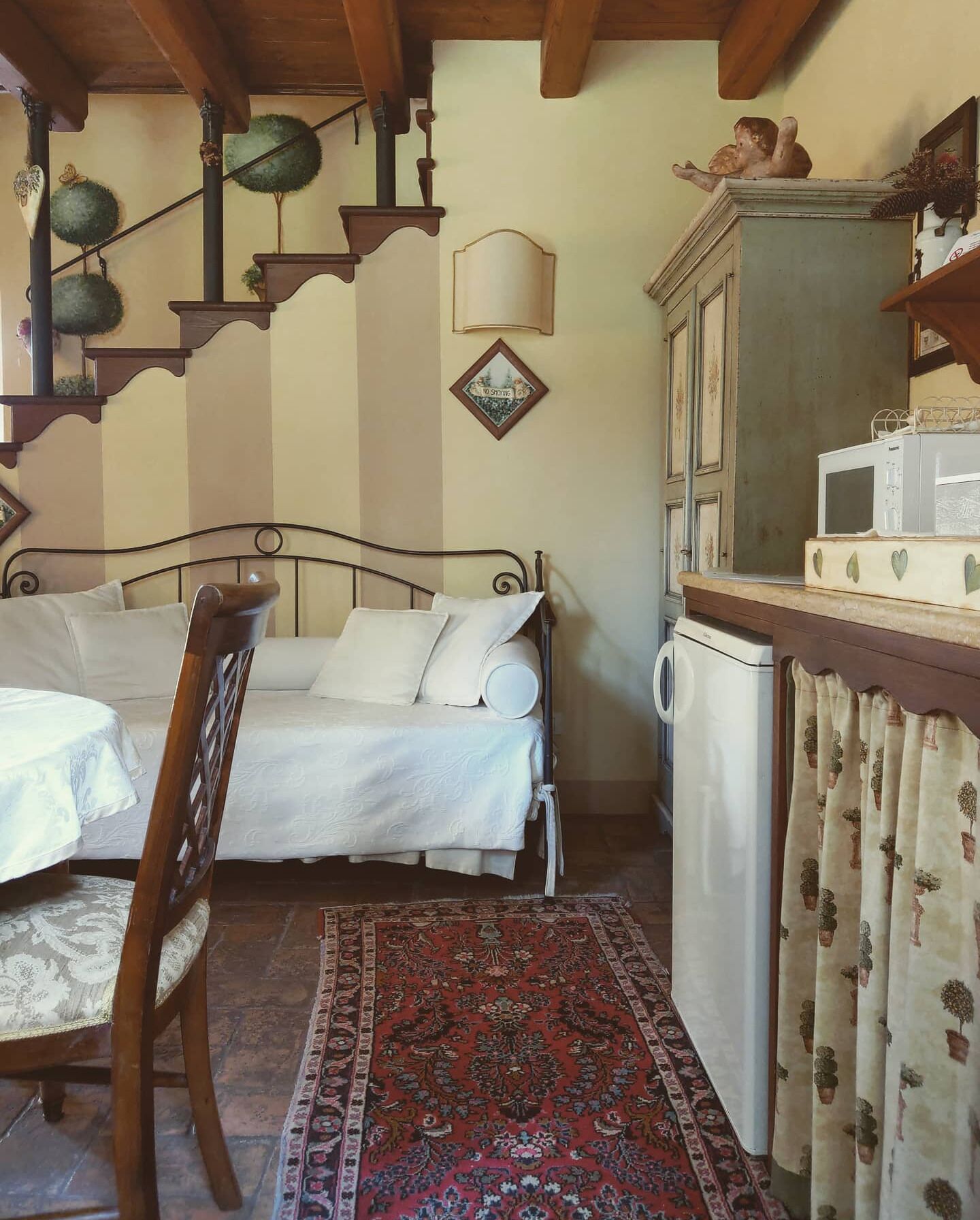 A cozy room with a bed, a dining table, a chair, a small refrigerator, a microwave, and a cabinet.