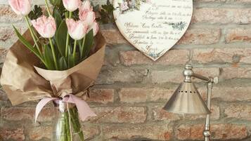 Un ramo de tulipanes rosados en un florero de cristal con envoltorio de papel marrón y una cinta rosa, una lámpara de pared de estilo vintage, y un letrero decorativo con forma de corazón con un mensaje.