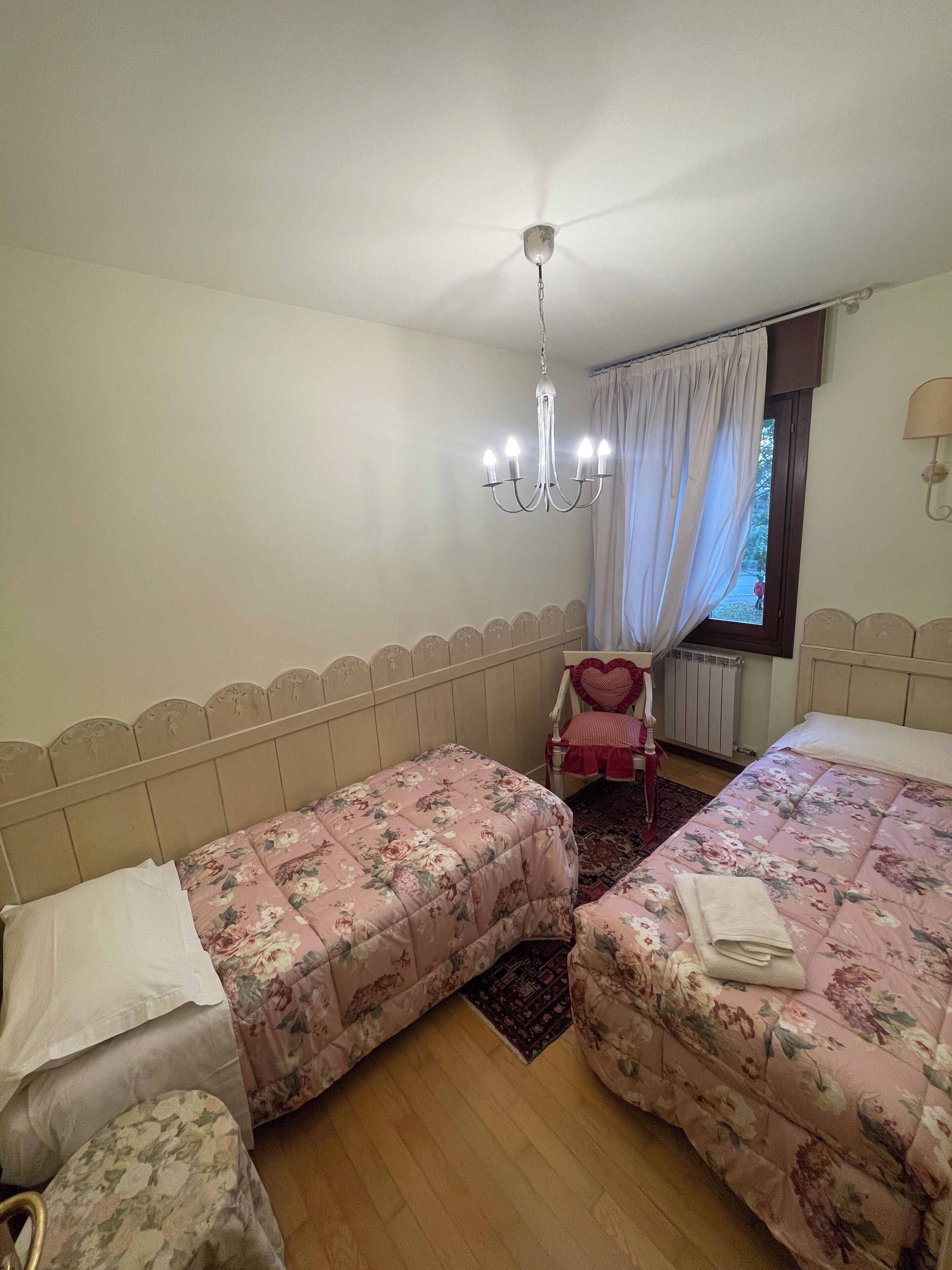 Ein Schlafzimmer mit zwei Betten, einer Kandelaberleuchte, einem Fenster mit Vorhängen und einer Heizung.