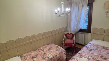 Ein Schlafzimmer mit zwei Betten, einer Kandelaberleuchte, einem Fenster mit Vorhängen und einer Heizung.