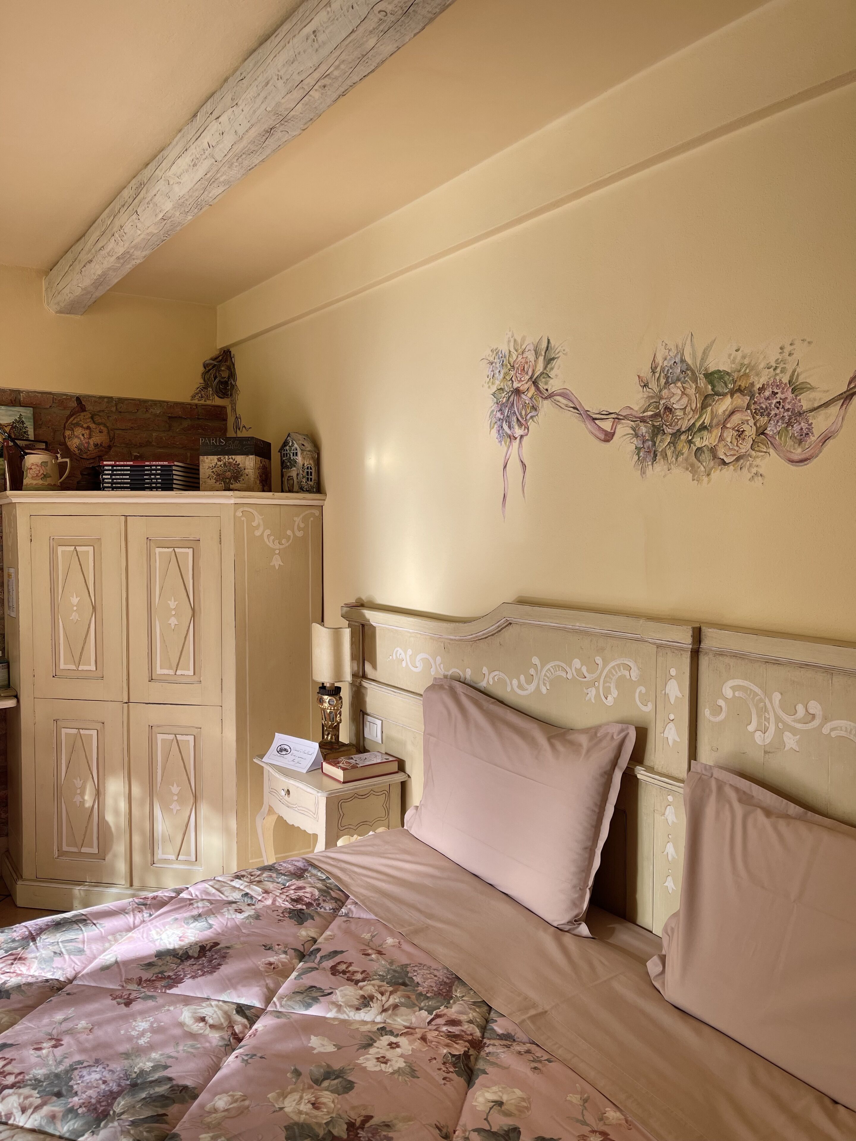 Ein Schlafzimmer mit Bett, Nachttisch, Kommode und einer Wand mit floralen Bildern.