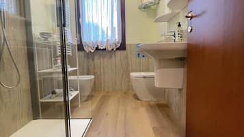 Un bany modern amb un plat de dutxa de vidre, un vàter, un rentapeus i una finestra amb cortines.