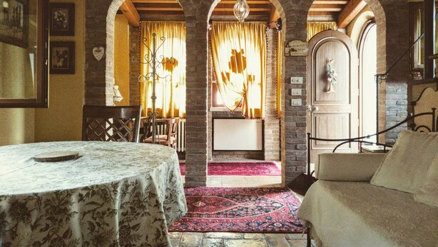 Una stanza con un tavolo, un divano, un tappeto decorato e una parete in mattoni con un arco.