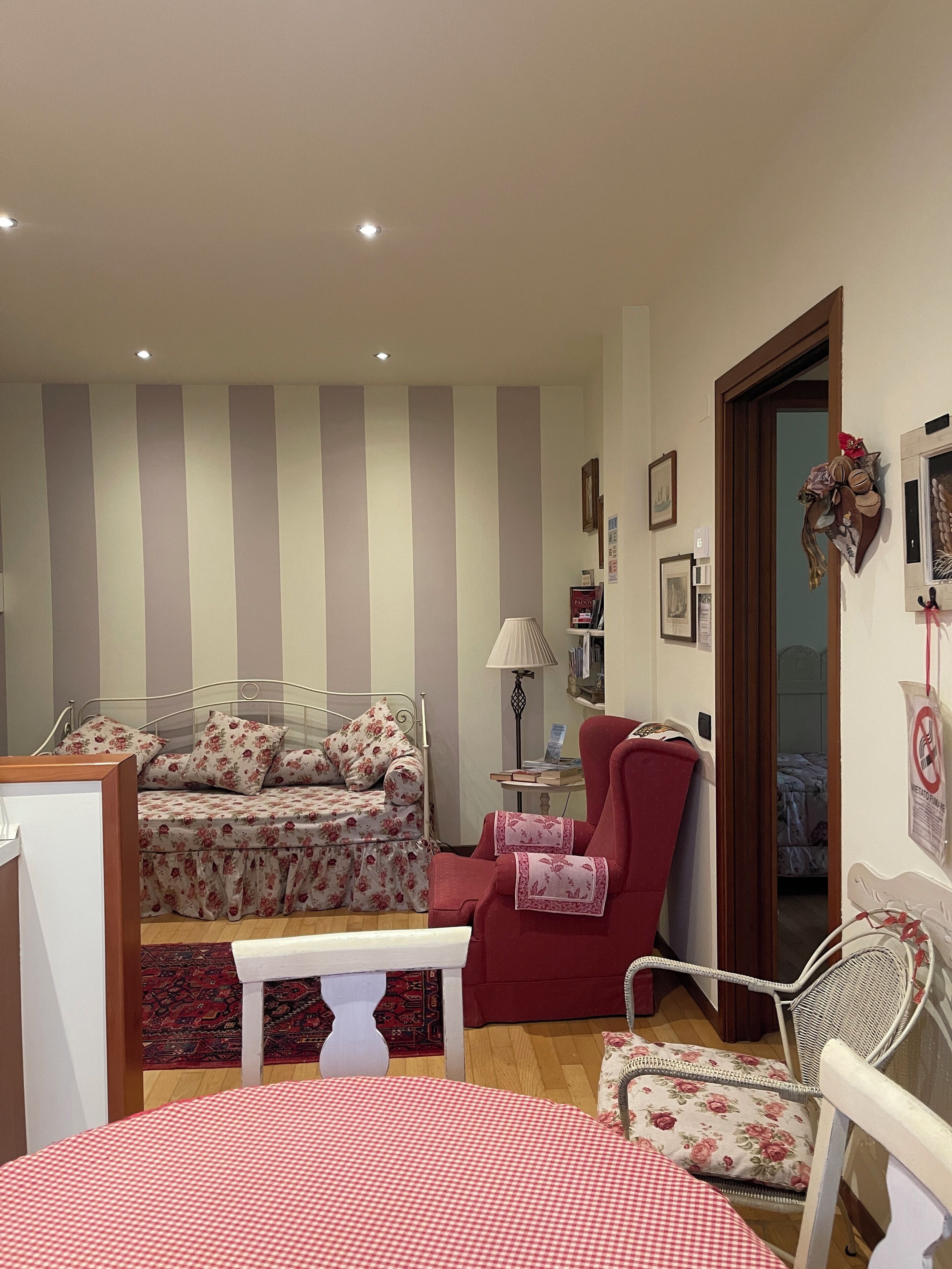 Une chambre à coucher avec un lit, un fauteuil rouge, une chaise blanche, une petite table et une porte donnant sur une autre pièce.