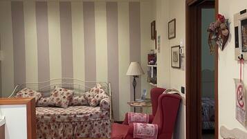 Une chambre à coucher avec un lit, un fauteuil rouge, une chaise blanche, une petite table et une porte donnant sur une autre pièce.