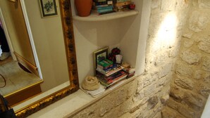 Una escalera con peldaños de madera y un muro de piedra. Se ve un espejo a la izquierda y una estantería con libros y un jarrón a la derecha.
