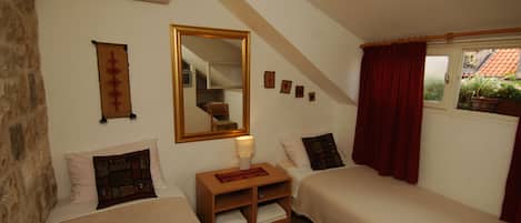 Un dormitorio con dos camas, un espejo, una mesita de noche y una ventana con cortinas rojas.