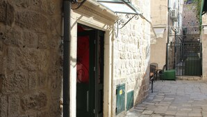 Una estrecha calle empedrada con la entrada de un edificio que tiene una puerta roja y una silla verde afuera.