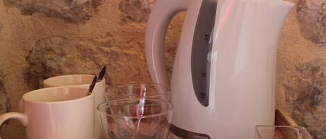 Una zona de cocina con un hervidor blanco, dos tazas y un vaso.