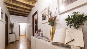 A hallway with wooden beams on the ceiling, a reception desk with brochures, a vase with flowers, and framed pictures on the wall. - Dulcis Inn Pantheon (Rome)