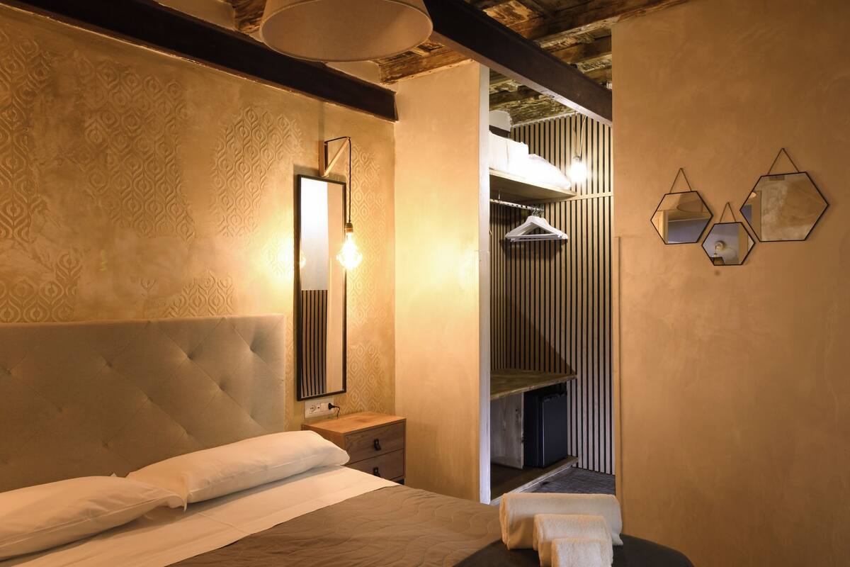 Un dormitorio con cabecera capitonada, una mesita de noche, una lámpara colgante y un espejo.