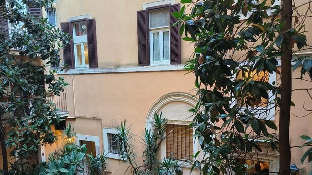 A courtyard with potted plants, a cobblestone path, and a building with balconies and shutters. - Dulcis Inn Pantheon (Rome)