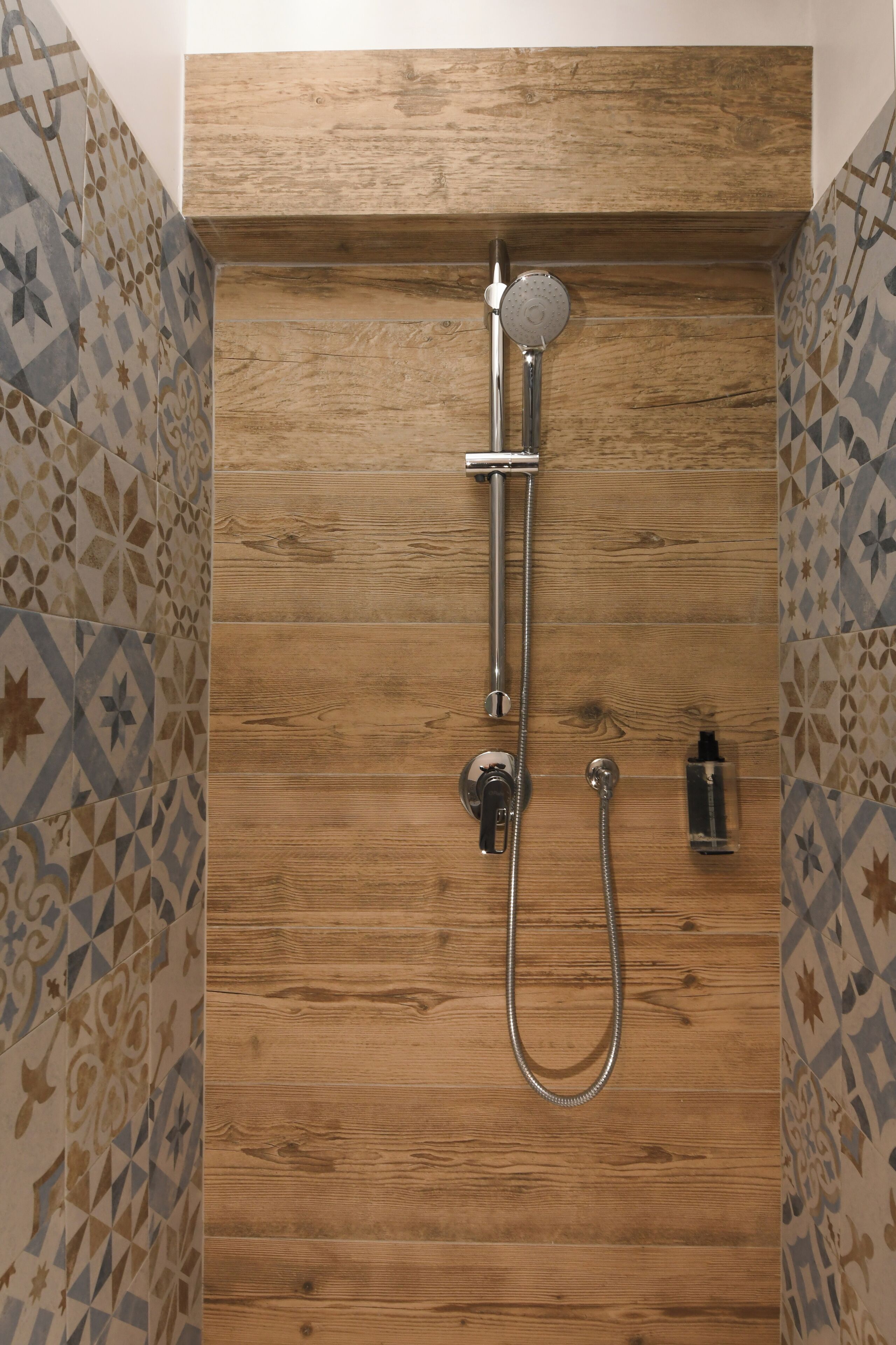 A shower with a wooden panel wall, a handheld showerhead, and a handheld shower attachment.