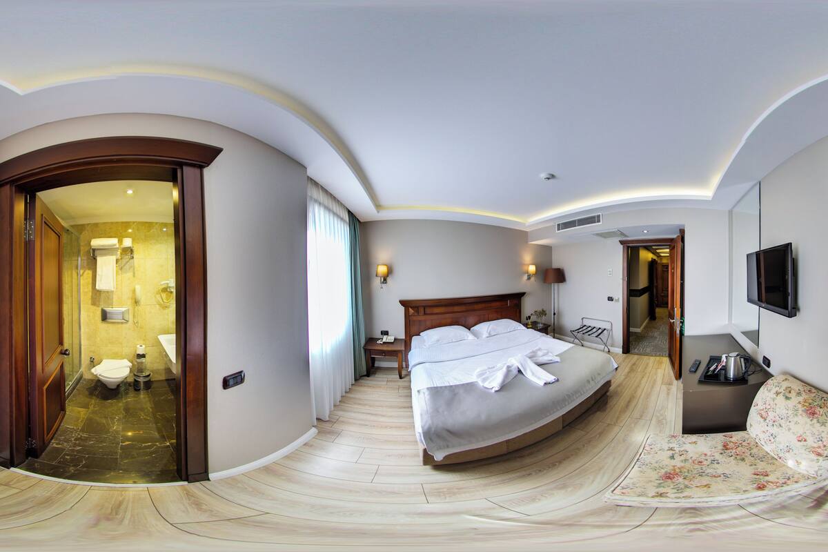 A modern hotel room with a curved ceiling, a large bed, a TV, and a bathroom visible through an open door.
