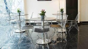 Uma sala de jantar moderna com mesas redondas e cadeiras de estrutura metálica, uma televisão na parede e um abajur.