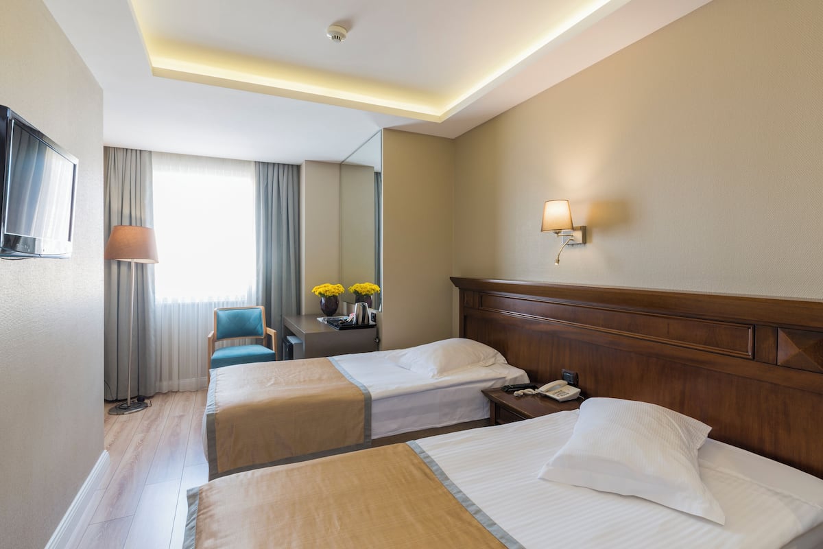 A hotel room with two beds, a desk with a lamp, a mirror, and a window with curtains.