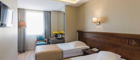 A hotel room with two beds, a desk with a lamp, a mirror, and a window with curtains.