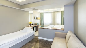 Quarto de hotel com cama, sofá, escrivaninha com cadeira e televisão.