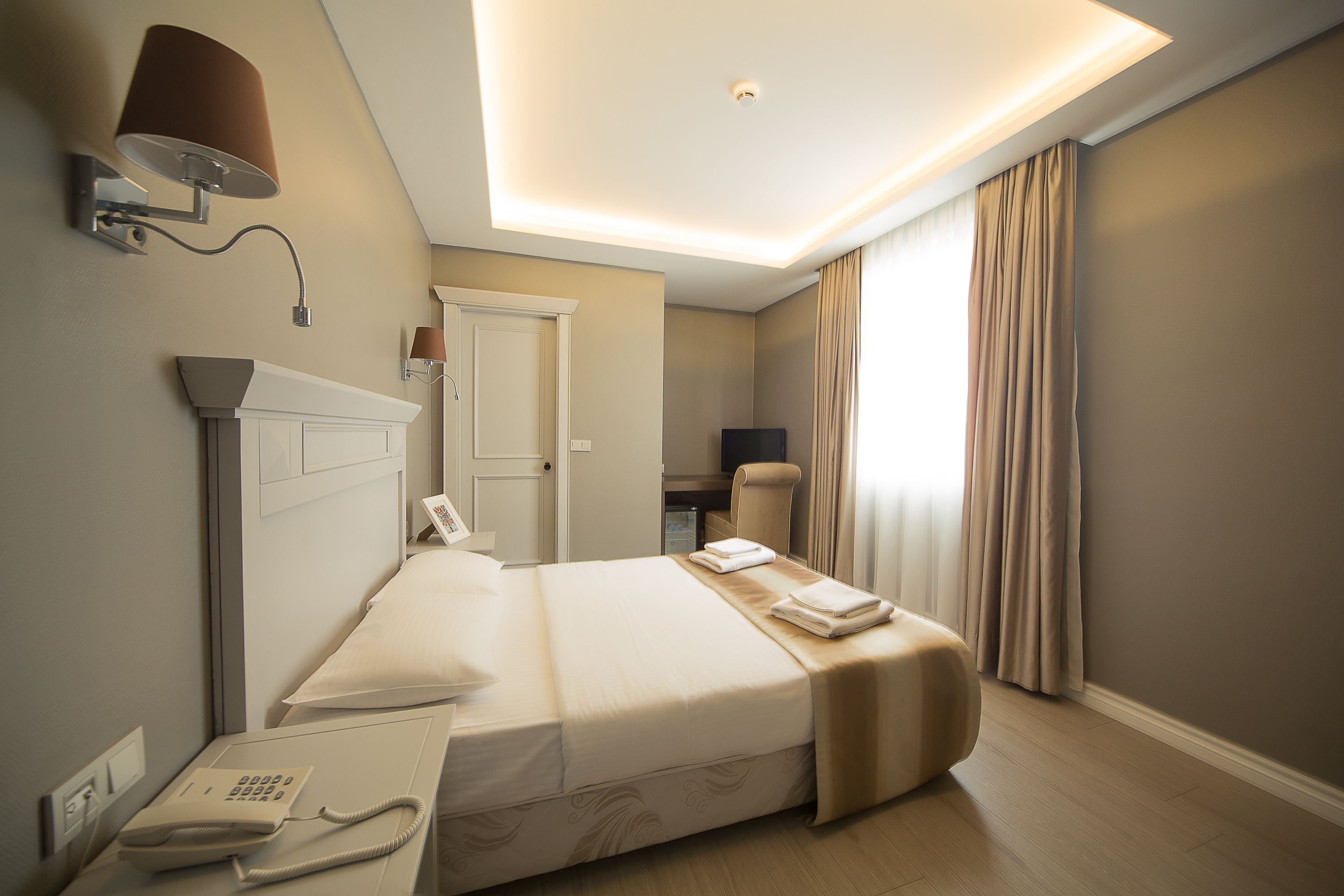 A hotel room with a bed, bedside lamp, telephone, and a desk with a chair.