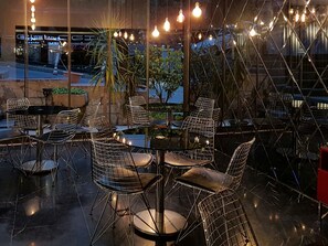 An outdoor seating area with metal wire chairs and tables, illuminated by hanging light bulbs. - Semsan Hotel (Istanbul)