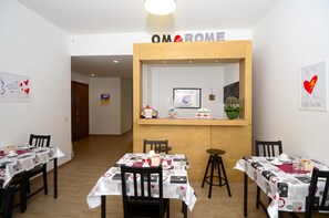 A dining area with tables set for four, a reception desk, and artwork on the walls. - OM2Rome (Rome)