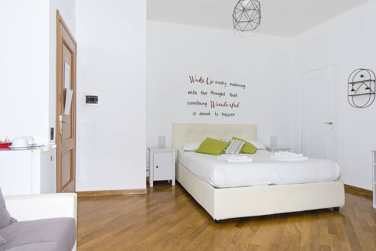 Een moderne slaapkamer met een bed, nachtkastjes, een wandklok en een motiverende quote.