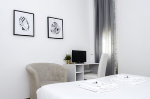 A hotel room with a bed, a chair, a desk with a TV, and two framed pictures on the wall. - OM2Rome (Rome)