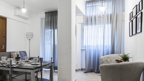 A modern living room with a dining area, featuring a sofa, a dining table with chairs, and a large window with curtains. - OM2Rome (Rome)