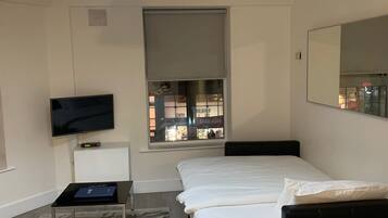 Una habitación de hotel moderna con una cama grande, televisión, escritorio y ventana con vista a la calle.