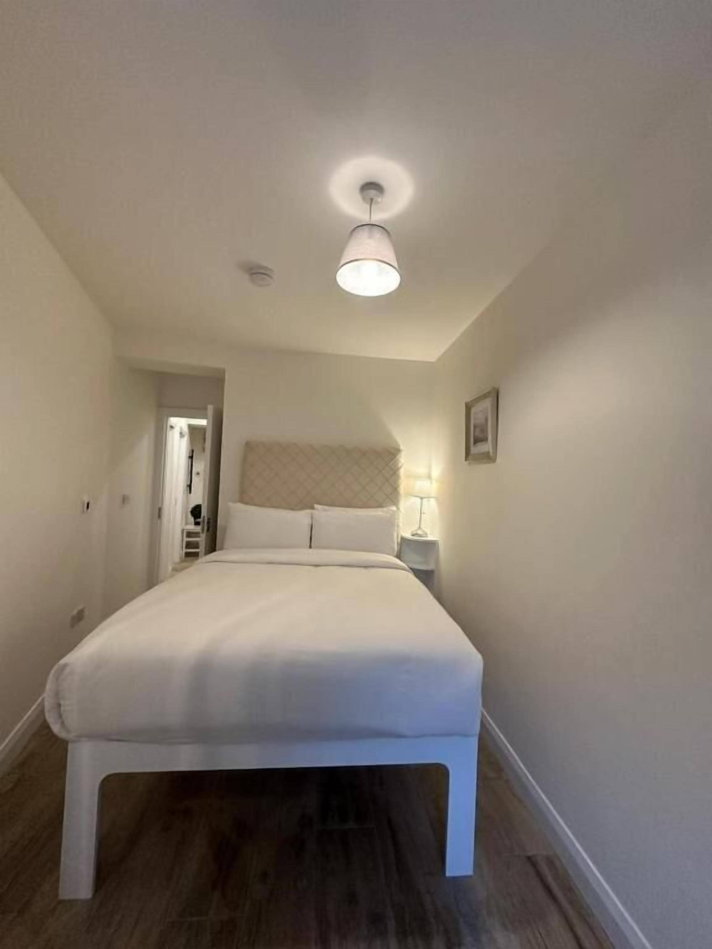 A bedroom with a large bed, a bedside table with a lamp, and a ceiling light.